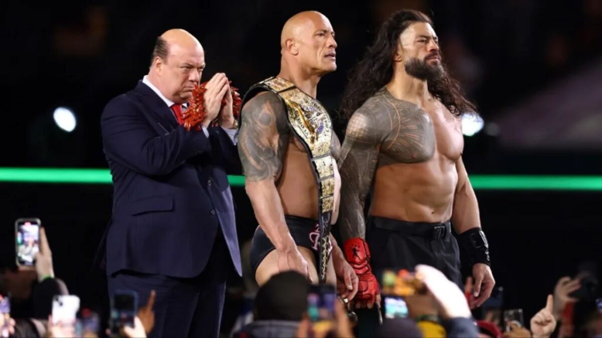 Paul Heyman standing beside The Rock and Roman Reigns
